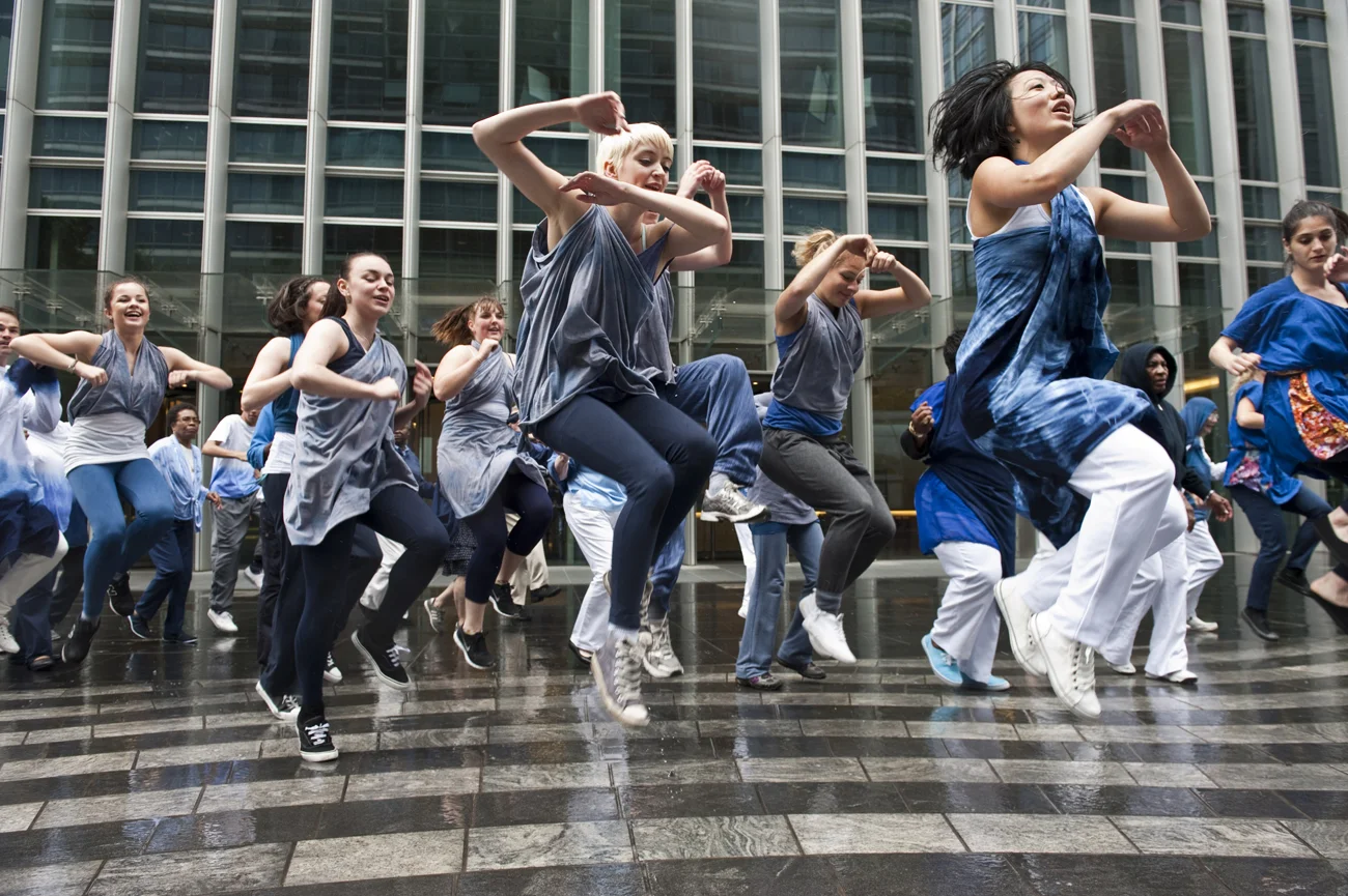 Dancers perform outdoors at Canary Wharf in front of a glass building.